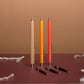 Three pens in beige, orange, and red on a brown surface with a brown background