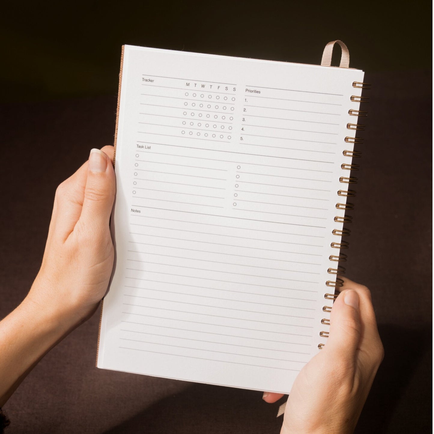 Person holding a spiral-bound planner with a dark background