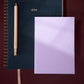 lavender planner with a pencil and blue notebook on a gradient background