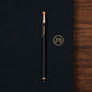 Navy pen with silver and gold accents on a navy surface with a wooden edge