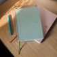 Two spiral-bound notebooks on a wooden surface with a pen next to them.